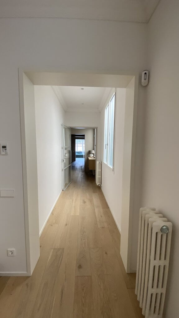 Pasillo reformado con suelo de madera natural y luz natural en vivienda de Muntaner