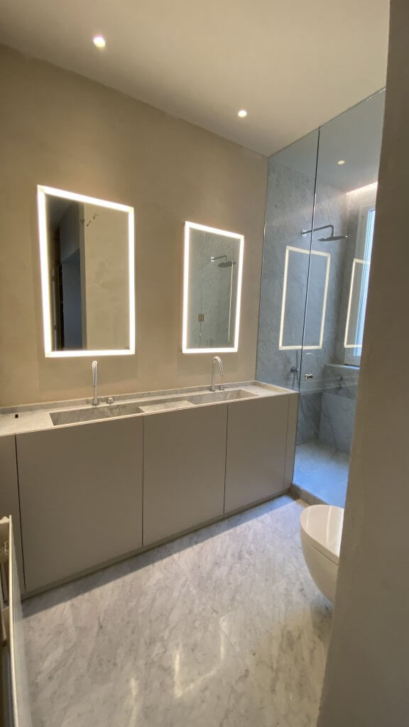 Baño doble con espejos retroiluminados y acabados en mármol en Muntaner Barcelona
