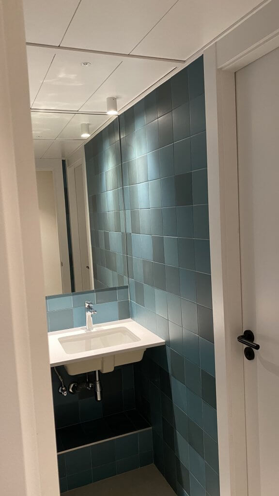 Baño con azulejos en tonos verdes y lavabo moderno suspendido
